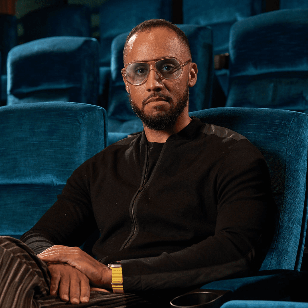 Image of a man sitting with his hands crossed on a blue velvet chair.