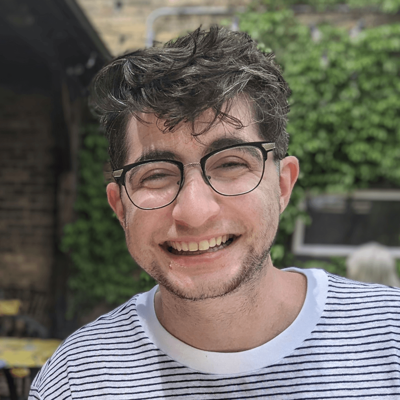 Portrait of a person with short hair wearing glasses and a black and white striped t-shirt.