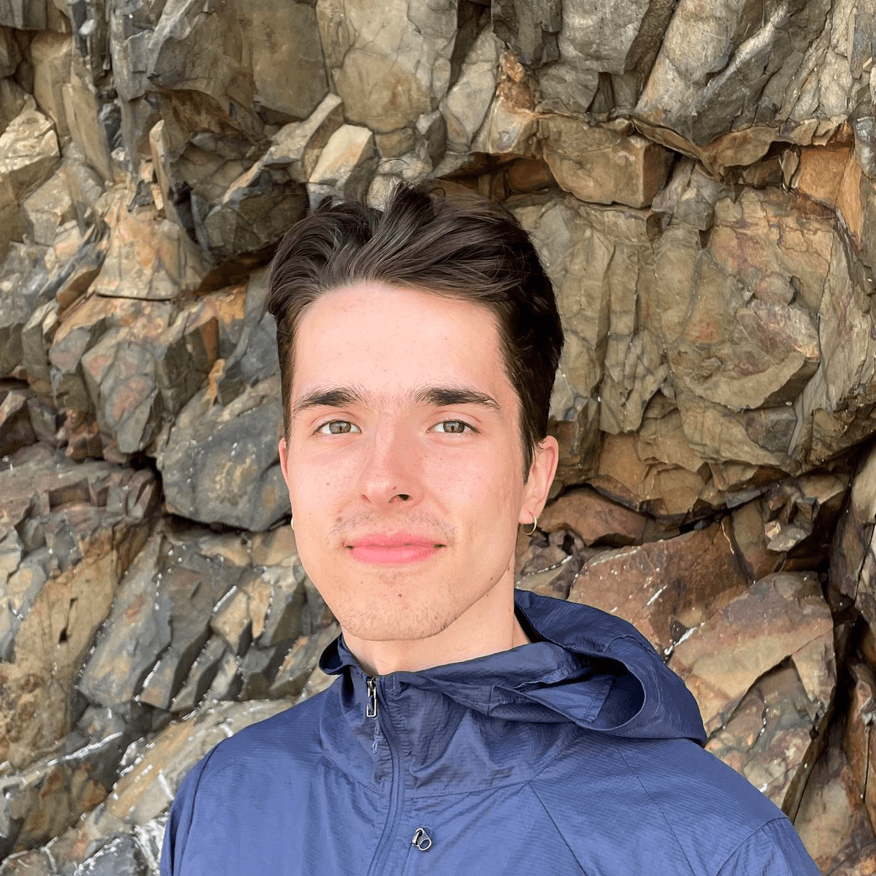 Man with brown hair slightly smiling on textured rock background